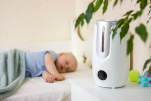 umidificador branco no quarto do bebe, com o bebe de roupinha azul dormindo ao fundo